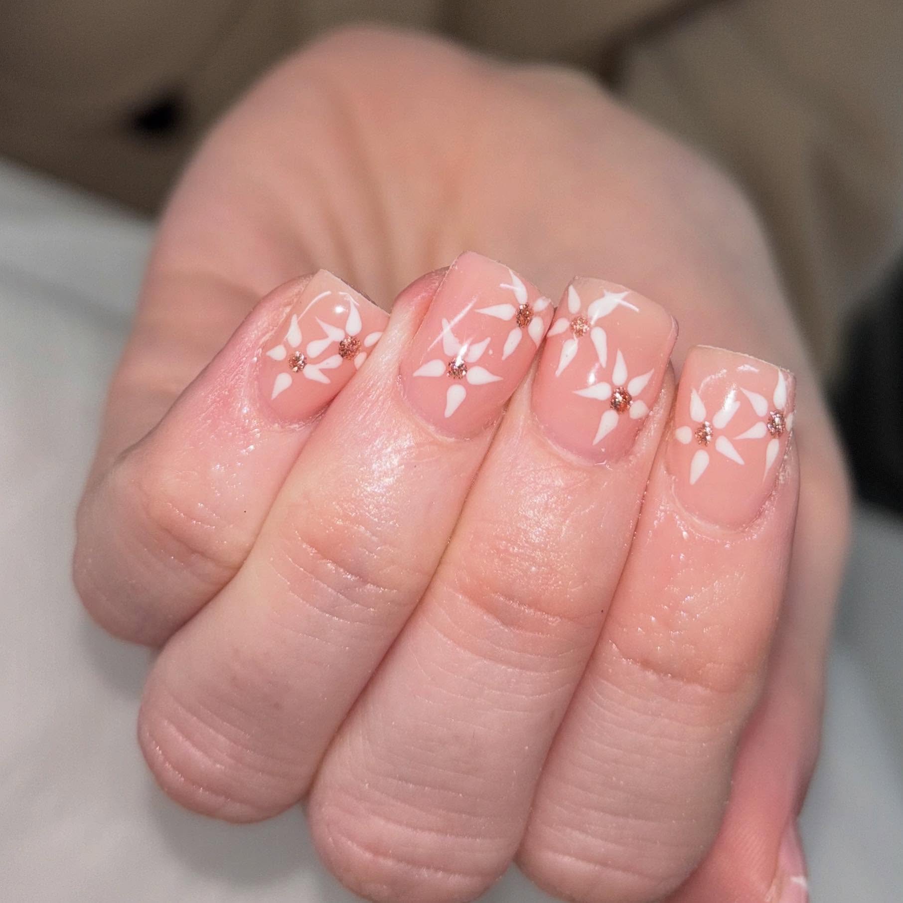 Nude pink nails with white floral art and rose gold gems